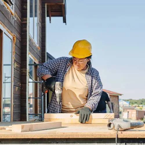 Construction worker using drill on wooden beam.