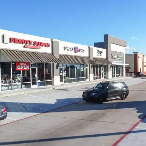 Strip mall storefronts with parked black SUV